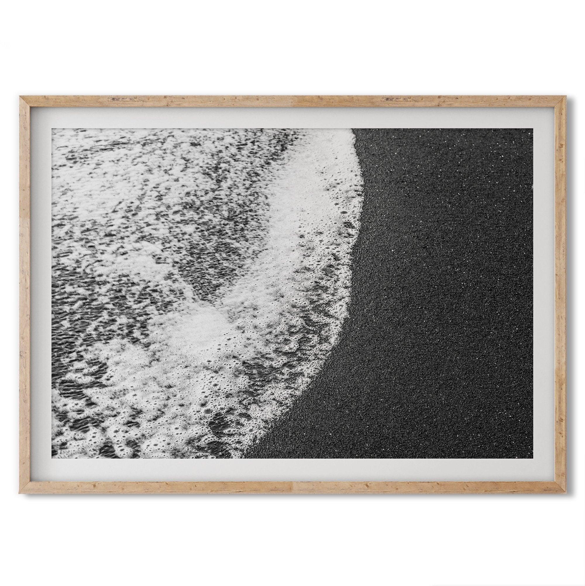 A minimalist fine art black and white beach print showing the ocean surf gently crashing onto a black sand beach in Maui, Hawaii.