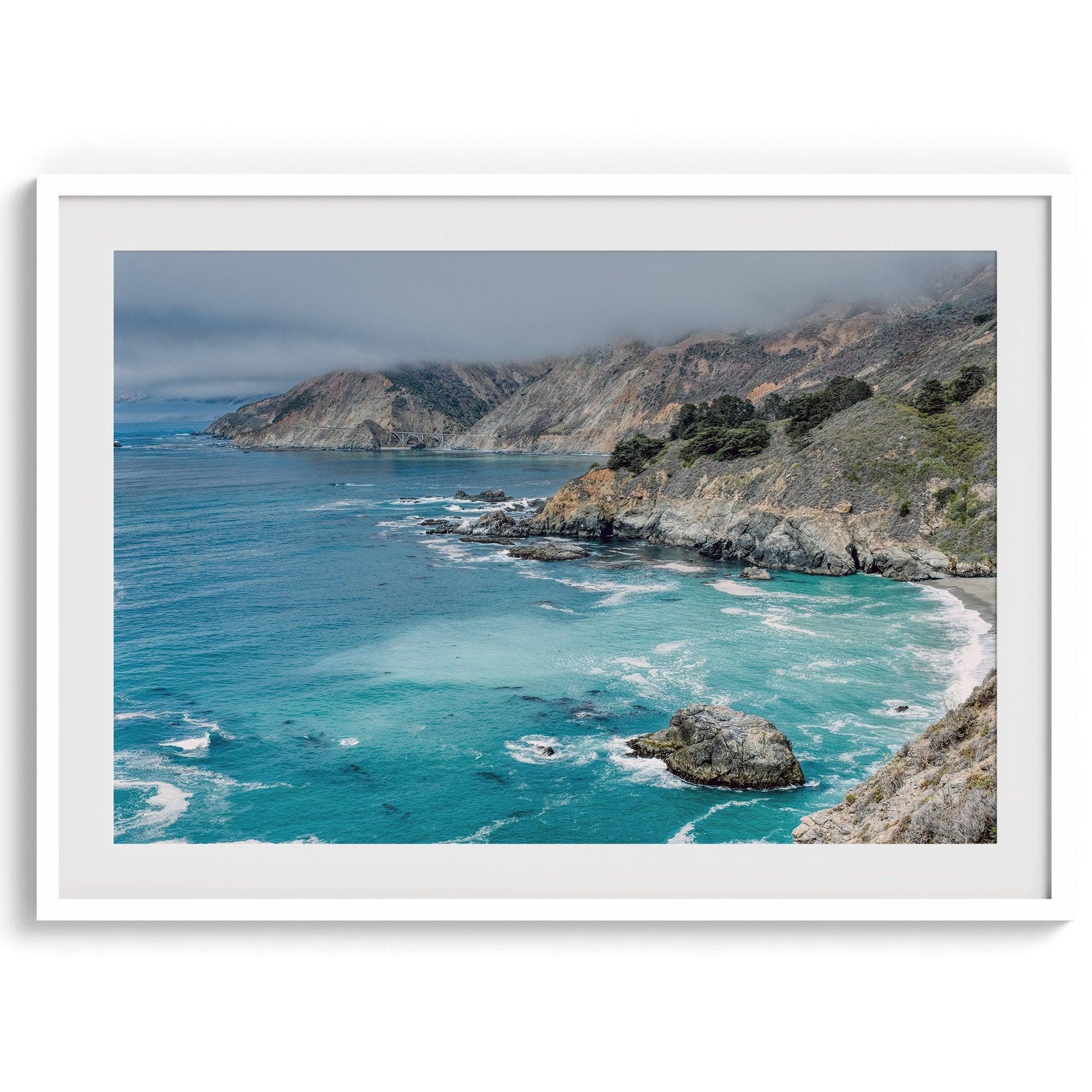 A fine art ocean print from Big Sur California featuring dramatic cliffs, the blue ocean and surf, and the Bixby bridge in the backdrop.