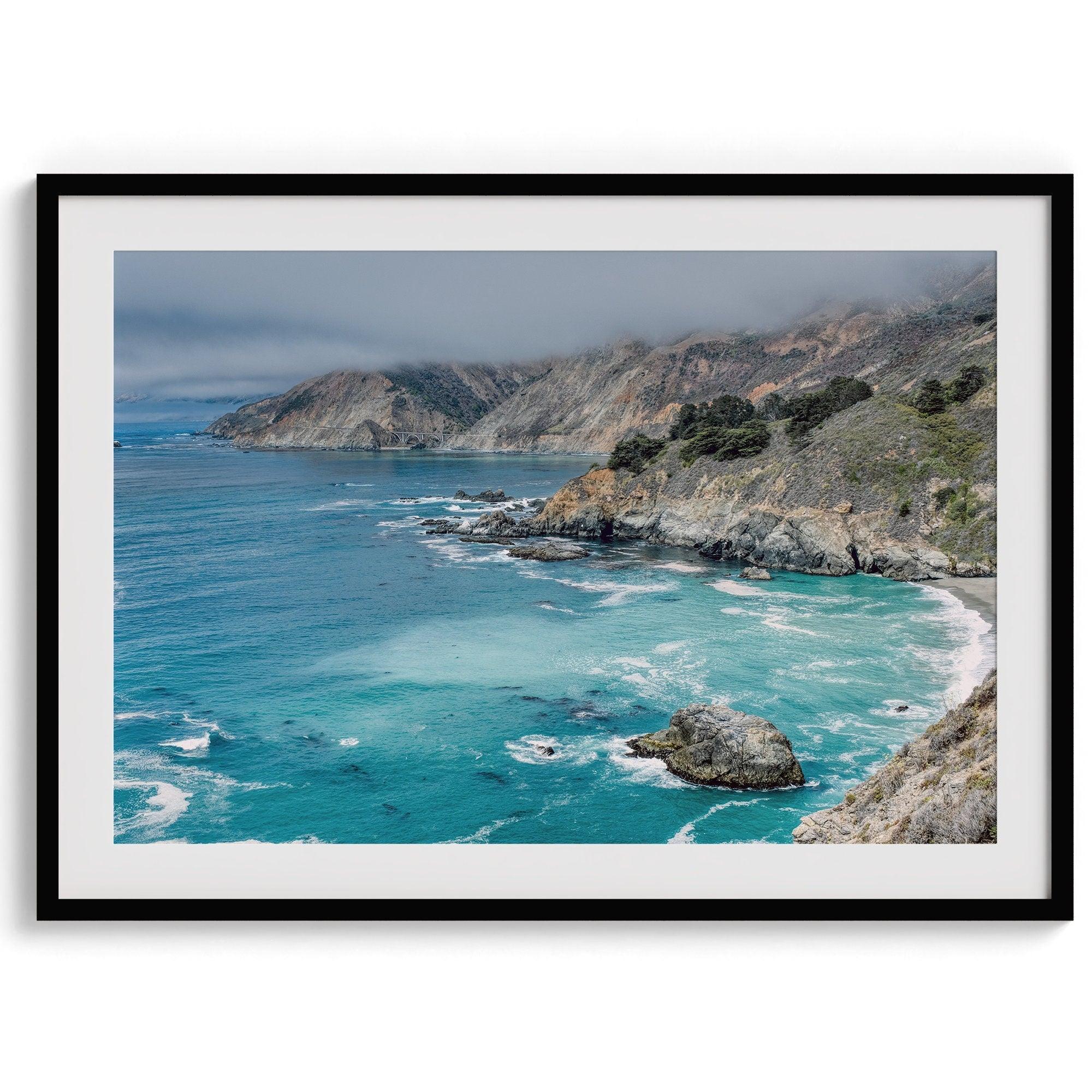 A fine art ocean print from Big Sur California featuring dramatic cliffs, the blue ocean and surf, and the Bixby bridge in the backdrop.