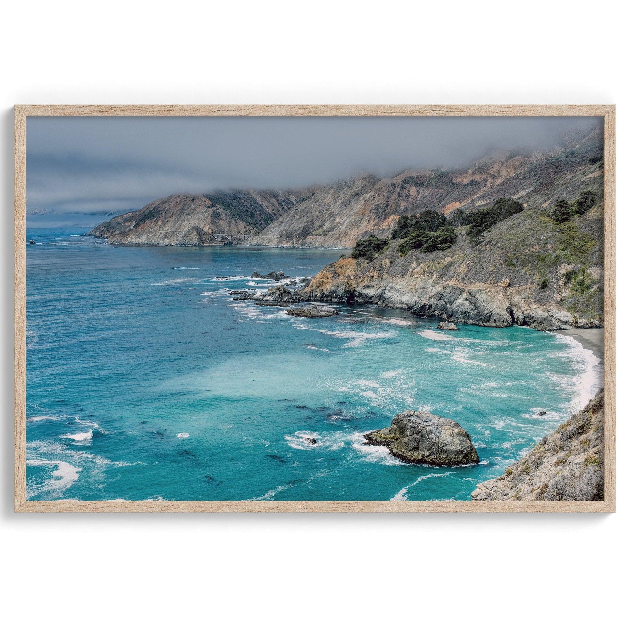 A fine art ocean print from Big Sur California featuring dramatic cliffs, the blue ocean and surf, and the Bixby bridge in the backdrop.