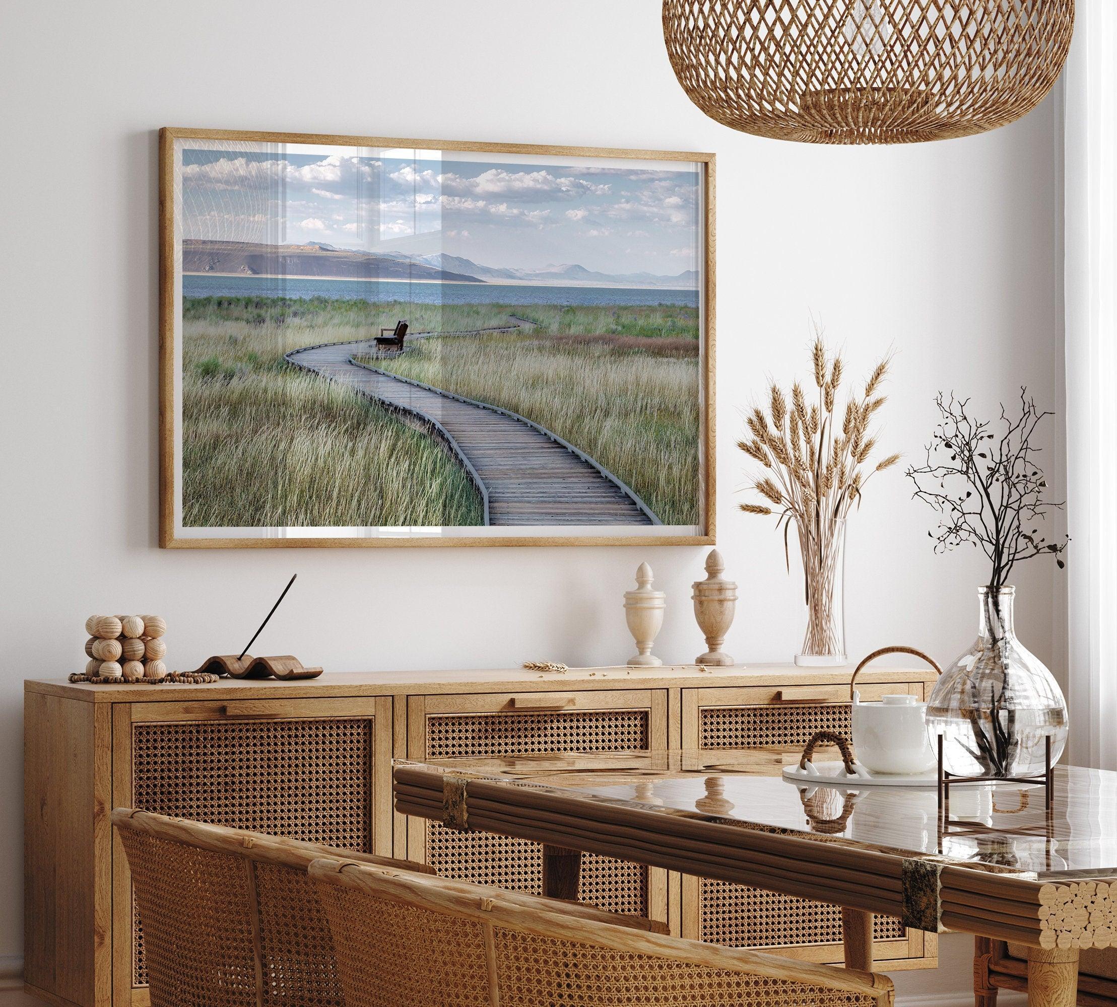 A fine art nature photography print featuring an inspiring winding path through the grassy wilderness of the eastern Sierra Nevada mountains toward Mono Lake. you can see the blue water of the lake in the background and a bench on the road.