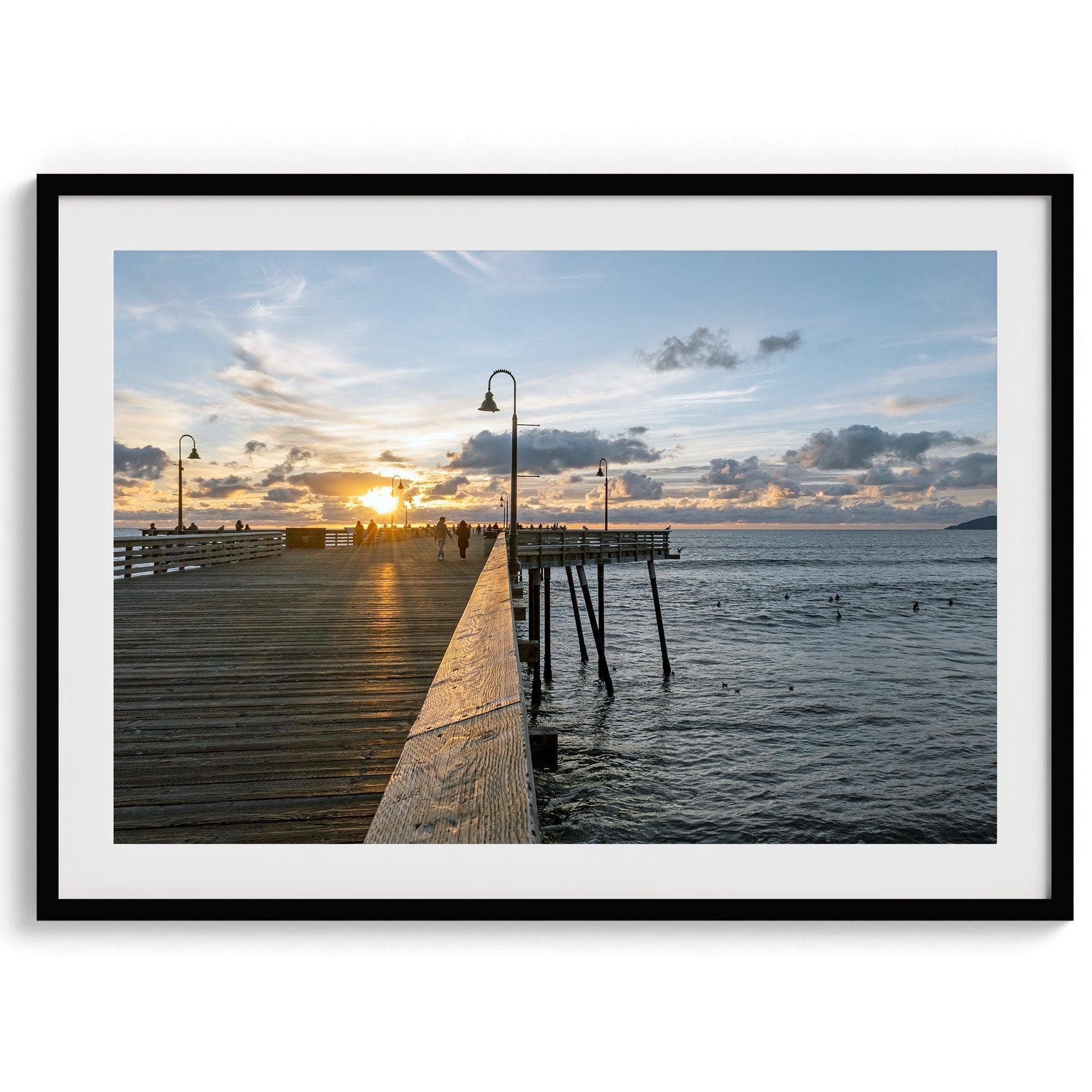 A fine art ocean sunset print featuring Pismo Beach Pier in Sunset with the surfers in the ocean and people enjoying a stroll on the pier.