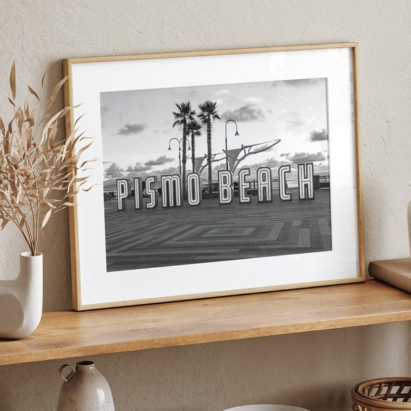 a fine art black and white modern beach print featuring the famous Pismo Beach sign in sunset with palm trees and the ocean in the backdrop,