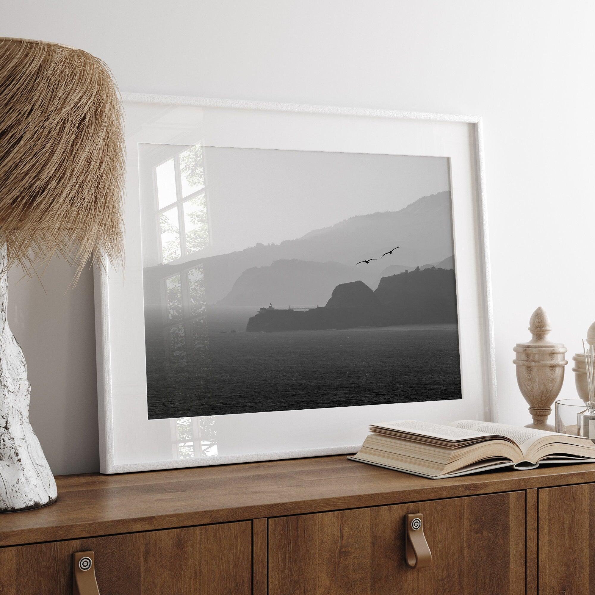 A black and white coastal wall art that showcases two Pelicans flying over the Pacific Ocean near the Golden Gate Bridge toward the layered mountains in the sunset.