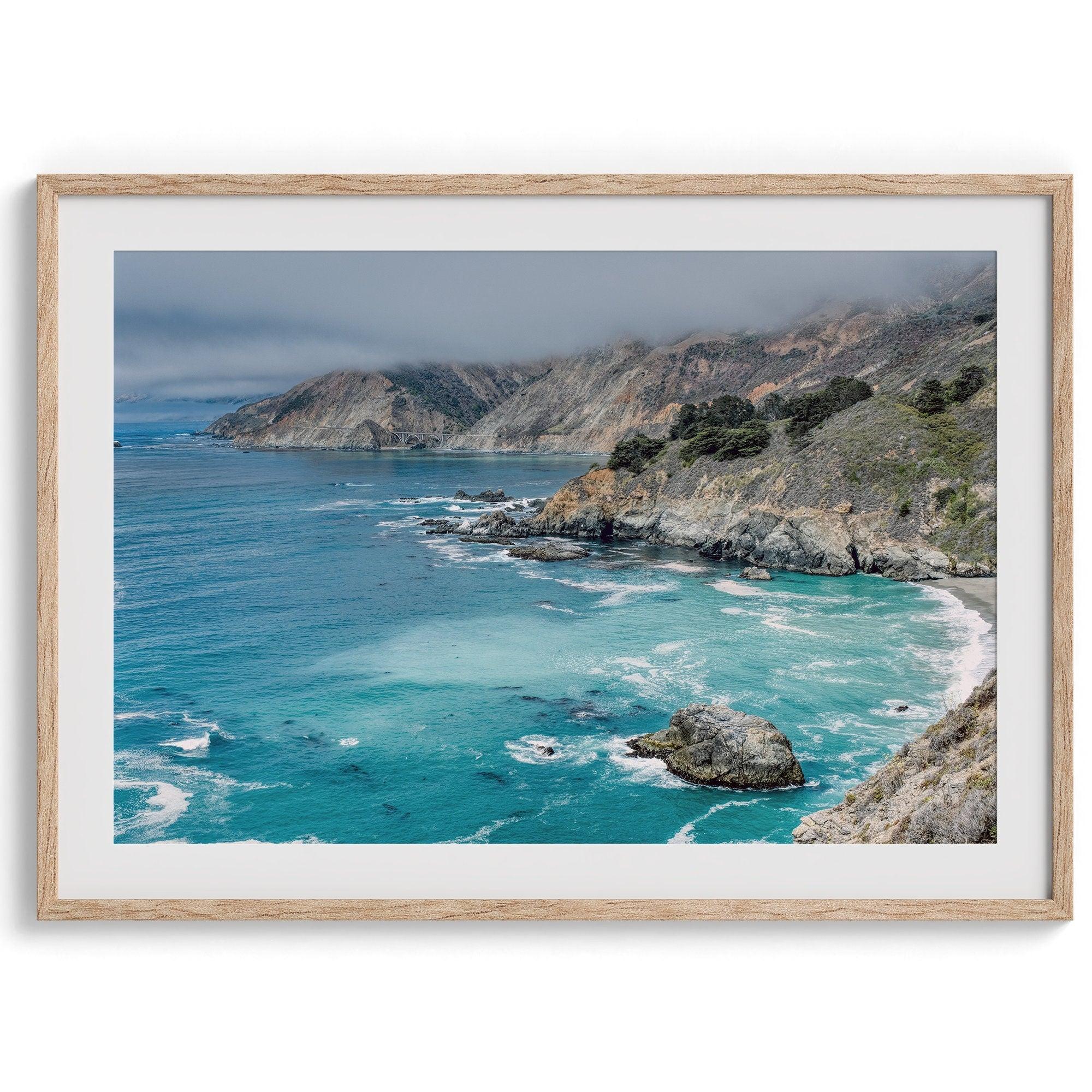 A fine art ocean print from Big Sur California featuring dramatic cliffs, the blue ocean and surf, and the Bixby bridge in the backdrop.