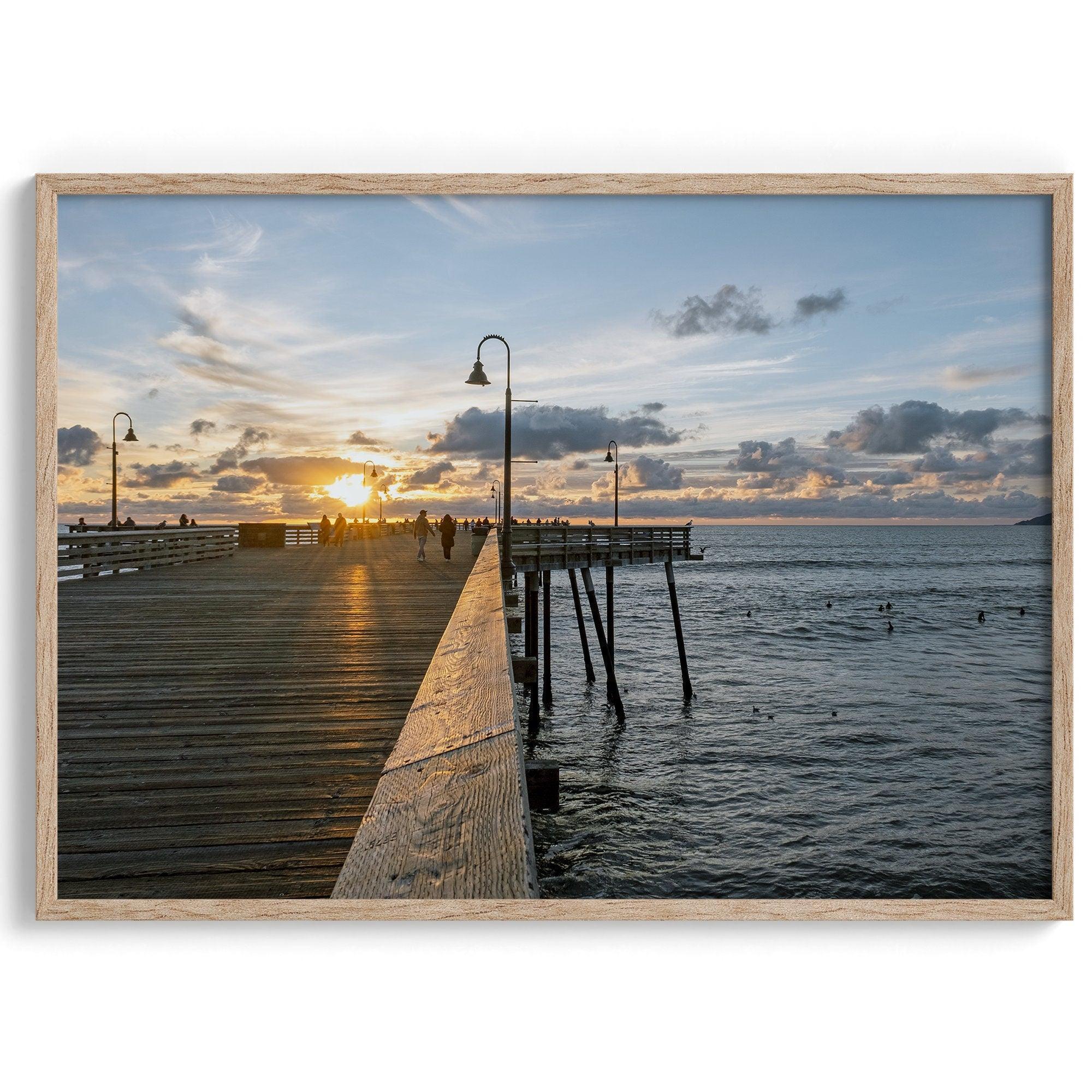 A fine art ocean sunset print featuring Pismo Beach Pier in Sunset with the surfers in the ocean and people enjoying a stroll on the pier.