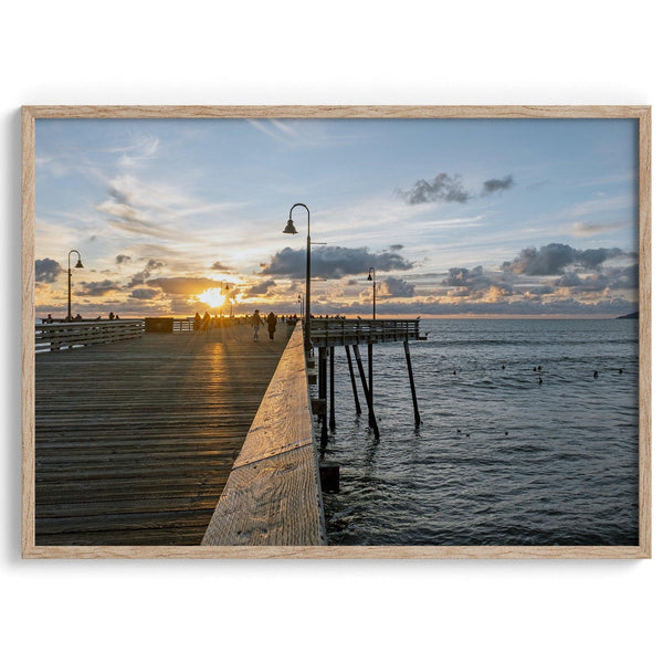 A fine art ocean sunset print featuring Pismo Beach Pier in Sunset with the surfers in the ocean and people enjoying a stroll on the pier.