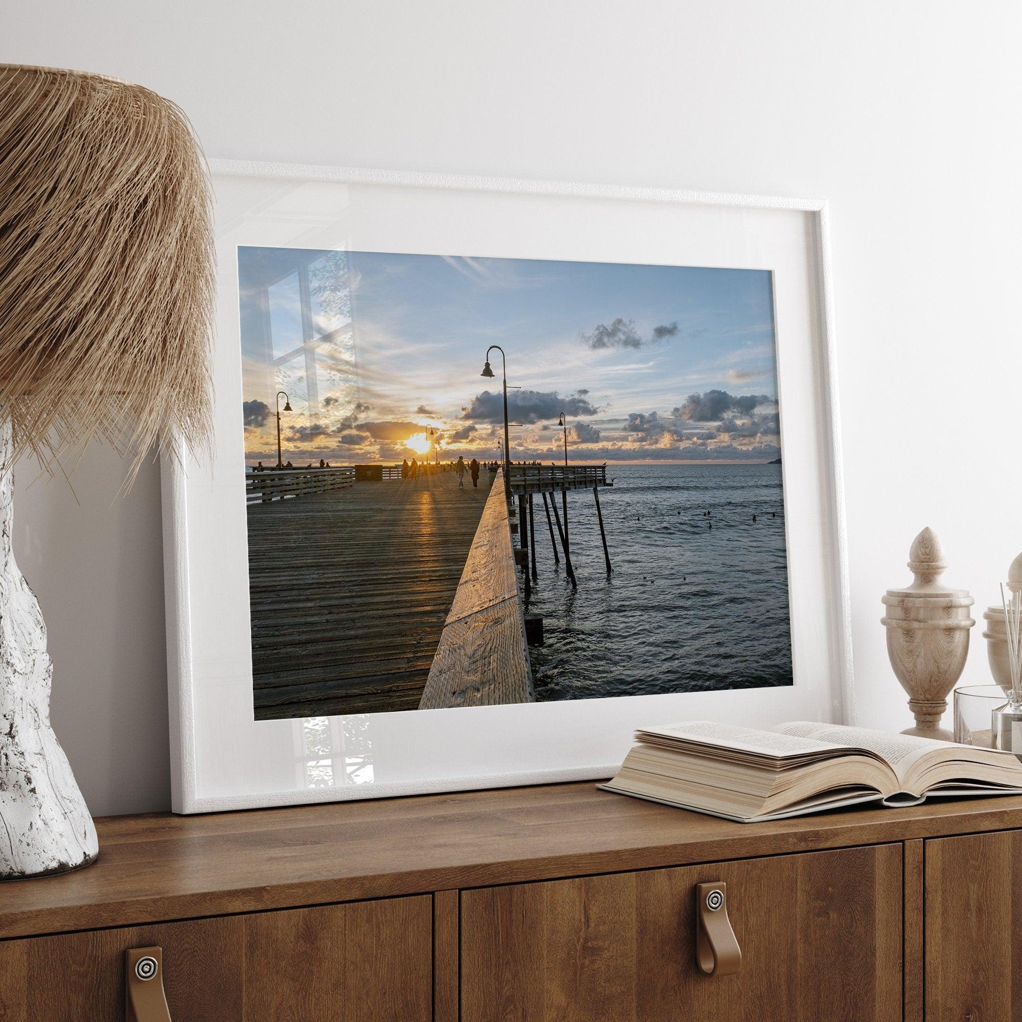 A fine art ocean sunset print featuring Pismo Beach Pier in Sunset with the surfers in the ocean and people enjoying a stroll on the pier.