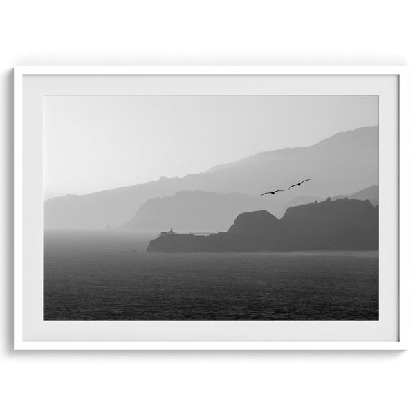 A black and white coastal wall art that showcases two Pelicans flying over the Pacific Ocean near the Golden Gate Bridge toward the layered mountains in the sunset.