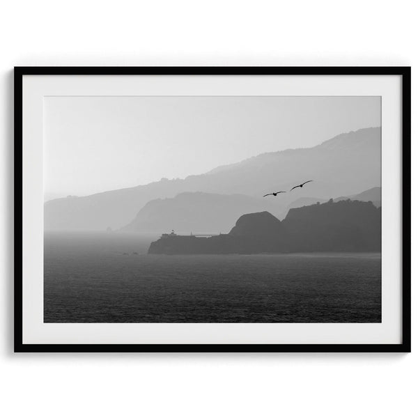 A black and white coastal wall art that showcases two Pelicans flying over the Pacific Ocean near the Golden Gate Bridge toward the layered mountains in the sunset.