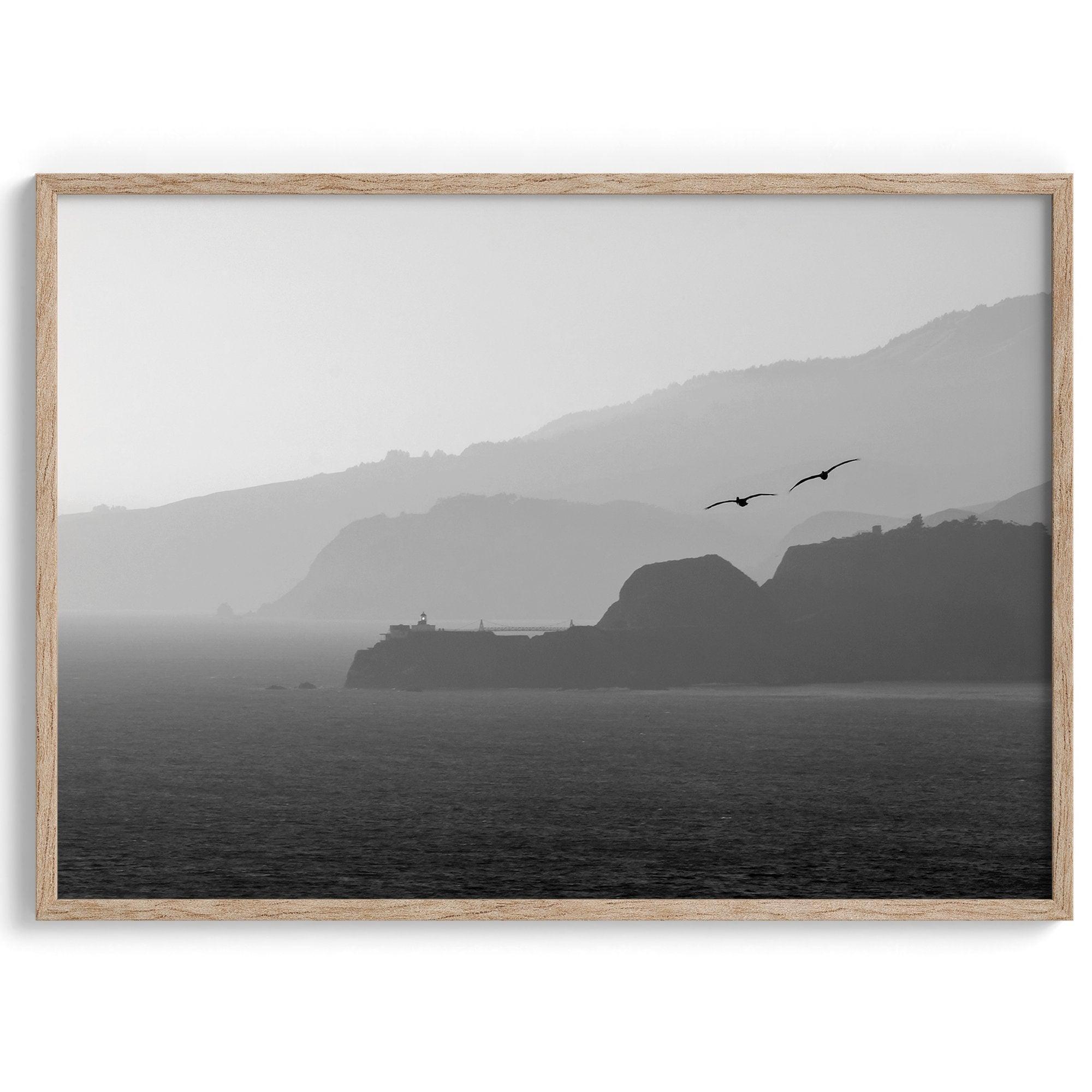 A black and white coastal wall art that showcases two Pelicans flying over the Pacific Ocean near the Golden Gate Bridge toward the layered mountains in the sunset.