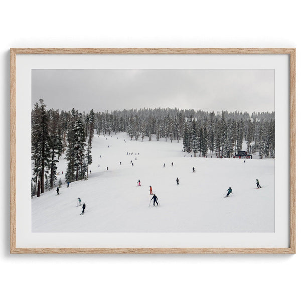 A fine art winter photography print of people skiing on the snow-covered Northstar Northern California mountain with snow-covered forest around.