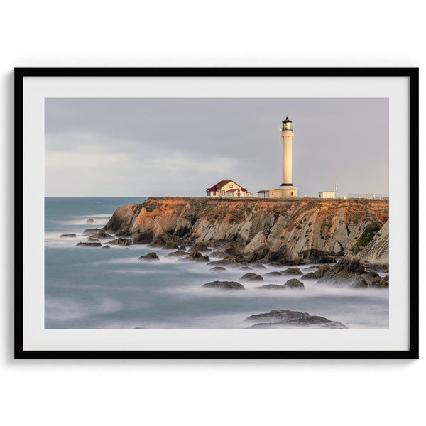 Long exposure fine art photography print of Pigeon Point Lighthouse at sunset. Golden light illuminates the lighthouse and cliffs, while the ocean surf crashes against the rocks in a creamy blur.