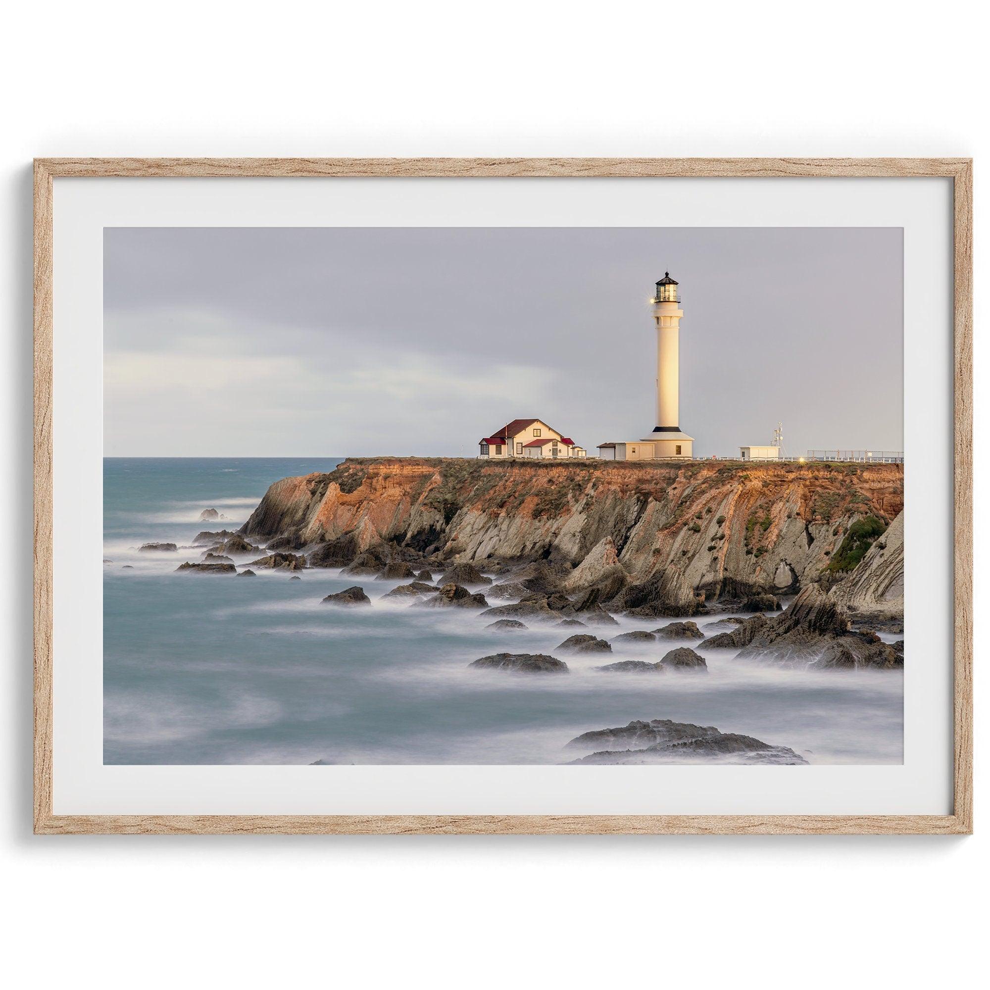 Long exposure fine art photography print of Pigeon Point Lighthouse at sunset. Golden light illuminates the lighthouse and cliffs, while the ocean surf crashes against the rocks in a creamy blur.